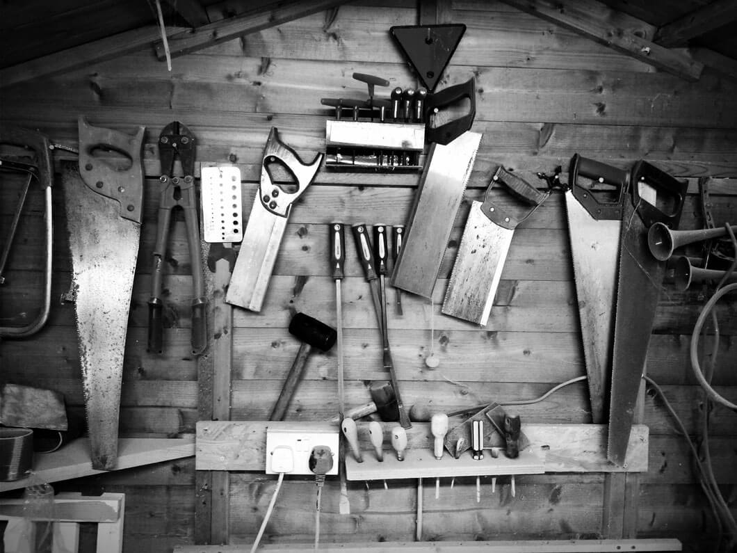 A gray-scaled full shot of tools for crafting wooden furniture is arranged on the wall.